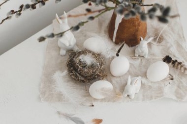 Paskalya kırsalında hayat. Doğal yumurtalar, tavşan heykelcikler, tüyler, yuva, eski ahşap masadaki vazoda söğüt dalları. Masada basit bir paskalya süsü var. Mutlu Paskalyalar