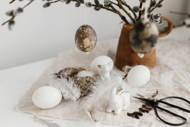 Paskalya kırsalında hayat. Doğal yumurtalar, tavşan heykelcikler, tüyler, yuva, eski ahşap masadaki vazoda söğüt dalları. Masada basit bir paskalya süsü var. Mutlu Paskalyalar