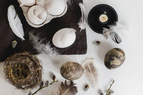 Paskalya kırsalının şık yatağı. Tepside doğal yumurtalar, tüyler, söğüt dalları, beyaz ahşap masadaki keten peçeteye yuva. Basit kırsal Paskalya natürmortu, pastel kahverengi renkte estetik.