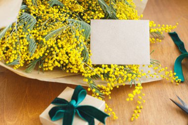 Mimoza buketi, hediye kutusu ve tahta arka planda tebrik kartı. Mutlu kadınlar günü ve mutlu anneler günü. Tebrik kartı şablonu metin için boşluk ile birlikte. 8 Mart kavramı
