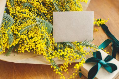 Mimoza buketi, hediye kutusu ve tahta arka planda tebrik kartı. Mutlu kadınlar günü ve mutlu anneler günü. Tebrik kartı şablonu metin için boşluk ile birlikte. 8 Mart kavramı