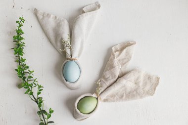 Paskalya yumurtalarını bahar çiçekli tavşan peçeteleri ve kırsal beyaz masa manzaralı yeşil dallı. Tatil masası düzenlemesi, kumaş dekorasyonunda doğal boya yumurtaları. Modern tablo ayarları