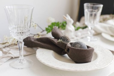 Tavşan peçetesinde paskalya yumurtası, çatal bıçak takımı, tavşan, kırsal beyaz masa üzerinde bahar çiçekleri. Zarif Paskalya brunch sofrası. Modern tablo düzenleme ve eko dekorasyon