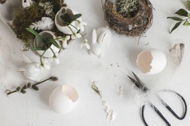 Paskalya yumurtası kabukları, çiçek açan kardelenler, tavşan heykelcikler, tüyler, eski beyaz ahşap masaya yuva. Paskalya kırsalının yaşam manzarası. Masada sade bir şenlik süsü var. Mutlu Paskalyalar!