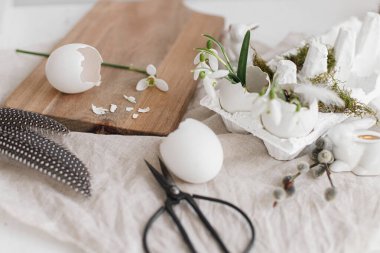 Paskalya kırsalında hayat. Paskalya yumurtası kabukları, çiçek açan kardelenler ve kırsal ahşap masada sevimli tavşan heykelciği. Masada sade bir şenlik süsü var. Mutlu Paskalyalar! Metin için boşluk