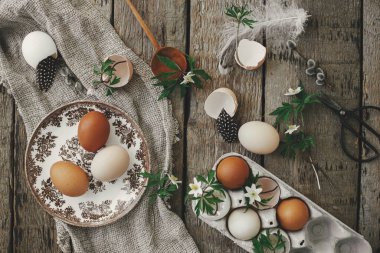 Mutlu Paskalyalar! Paskalya kırsalında hayat. Doğal paskalya yumurtaları, çiçek açan bahar çiçekleri, çuval bezi ve kaşık düz kırsal ahşap masa üzerinde yatıyordu. Masada basit bir şenlik dekorasyonu.