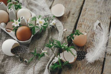 Paskalya kırsalında hayat. Doğal paskalya yumurtaları, çiçek açan bahar çiçekleri, tüyler, kırsal ahşap masada çuval bezi. Mutlu Paskalyalar! Masada basit bir şenlik dekorasyonu.
