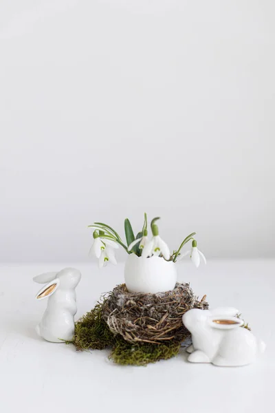 イースター素朴な静物画 白い木製のテーブルの上に巣とかわいいウサギの置物に開花する雪滴とイースターエッグシェル テーブルの上でスタイリッシュなお祝いの装飾 ハッピーイースター テキストのスペース — ストック写真
