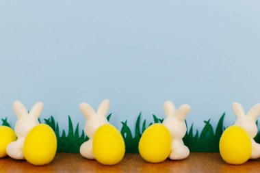 Mutlu Paskalyalar! Renkli Paskalya tavşanları ve çimenlerdeki yumurtalar mavi arka planda, mesaj için yer var. Beyaz ve sarı yapay dekor. Paskalya avı konsepti