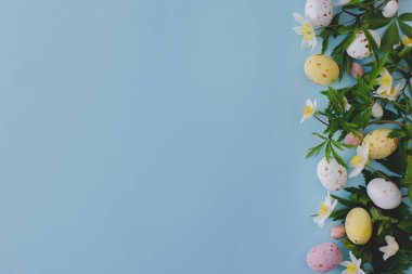Renkli Paskalya çikolatası yumurtaları ve bahar çiçekleri mavi arka planda, düz bir zeminde yazılı. Paskalya tebrik kartı şablonu. Mutlu Paskalyalar!