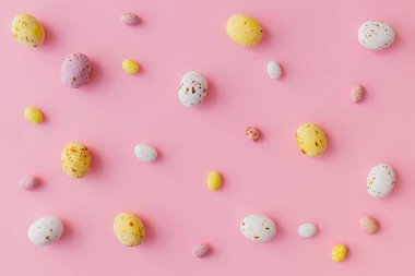 Paskalya düzlüğü. Renkli Paskalya çikolatası yumurtaları pembe arka planda yatıyordu. Paskalya arkaplanı ve tebrik kartı. Mutlu Paskalyalar! Beyaz, pembe ve sarı şeker düzeni