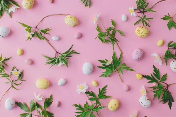 カラフルなイースターチョコレートの卵とピンクの背景に春の花のレイアウト ハッピーイースター スタイリッシュなイースターフラットレイ グリーティングカードまたはバナー — ストック写真