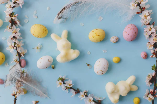 ハッピーイースター カラフルなイースターチョコレートの卵 ウサギ 青い背景に羽のレイアウト イースター フラット グリーティングカードやバナー スタイリッシュな春イメージ — ストック写真