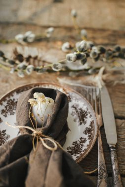 Rustic Easter table setting. Natural egg in napkin with flowers, setting  with vintage plate, cutlery, pussy willow branches on aged wooden table. Easter table decoration
