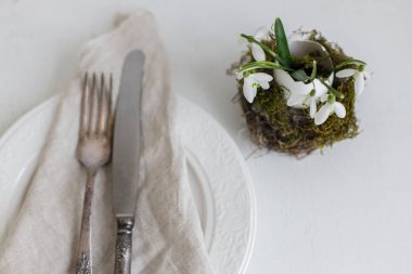 Üst görünümü ayarlayan şık Paskalya masası. Yuvasında kar damlası olan doğal yumurta, modern tabak, peçete, beyaz ahşap çatal bıçak takımı. Modern Paskalya sofrası sade dekorasyonu