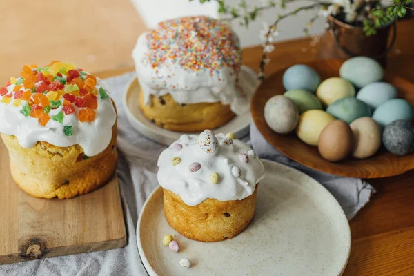 Homemade easter breads, natural dyed eggs and spring blossom on rustic table in room. Happy Easter! Freshly baked easter cakes with sugar glaze and sprinkles, traditional ukrainian bun