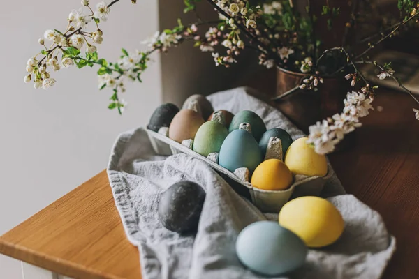 复活节快乐 复活节彩蛋放在带有樱花的乡村餐桌上 在木制板上的纸盘上 用亚麻布餐巾和春花把彩蛋自然染成彩色 乡村静谧的生活 — 图库照片