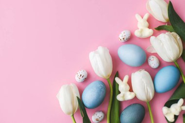 Paskalya yumurtaları, laleler ve tavşanlar pembe arka planda yatıyordu. Modern doğal boyanmış paskalya yumurtaları ve beyaz laleler. Tebrik kartı şablonu, metin için boşluk. Renkli paskalya arkaplanı