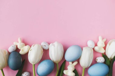 Paskalya yumurtaları, laleler ve tavşanlar pembe arka planda yatıyordu. Modern doğal boyanmış paskalya yumurtaları ve beyaz laleler. Tebrik kartı şablonu, metin için boşluk. Renkli paskalya arkaplanı
