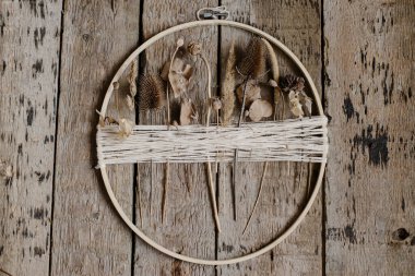 Kuru çiçeklerle süslenmiş şık bir sonbahar çelengi. Ahşap halka, iplik ve sade otlar kırsal ahşap arka planda. Modern çiçek düzenleme ve el yapımı dekorasyon