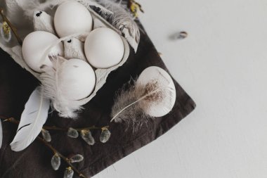 Paskalya sade estetiği. Tepside doğal yumurtalar, tüyler, söğüt dalları beyaz ahşap masada sade keten peçete. Kırsal Paskalya pastel beyaz ve kahverengi renklerde sakin bir hayat