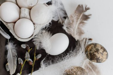 Paskalya sade estetiği. Tepside doğal yumurtalar, tüyler, söğüt dalları beyaz ahşap masada sade keten peçete. Kırsal Paskalya pastel beyaz ve kahverengi renklerde sakin bir hayat