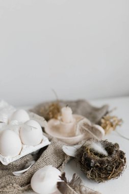 Tepside doğal paskalya yumurtaları, tüyler, söğüt dalları, beyaz ahşap masada çuval bezi üzerine yuva. Paskalya kırsalında hayat. Pastel bej renklerinde basit kırsal Paskalya estetiği. Mutlu Paskalyalar