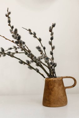 Modern rustic Easter still life. Willow branches in stylish vase on wooden table. Pussy willow branches in home, natural spring decor. Simple Easter rural minimal aesthetics. Space for text