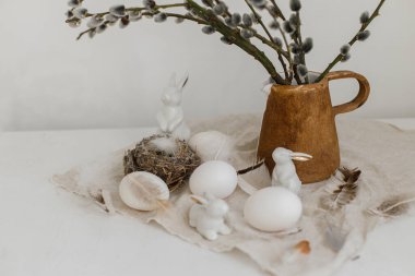 Paskalya kırsalında hayat. Doğal yumurtalar, tavşan heykelcikler, tüyler, yuva, eski ahşap masadaki vazoda söğüt dalları. Masada basit bir paskalya süsü var. Mutlu Paskalyalar