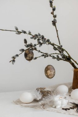 Paskalya kırsalında hayat. Doğal yumurtalar, tavşan heykelcikler, tüyler, yuva, eski ahşap masadaki vazoda söğüt dalları. Masada basit bir paskalya süsü var. Mutlu Paskalyalar