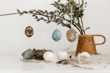 Paskalya kırsalında hayat. Doğal boyalı paskalya yumurtaları, vazodaki söğüt dalları, tüyler, eski ahşap masadaki keten peçeteye yuva. Mutlu Paskalyalar! Masa estetiği üzerine basit bir paskalya süslemesi.