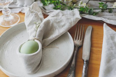 Mutlu Paskalyalar! Tavşan peçetesindeki paskalya yumurtası tabakta çatal bıçak, tavşan, bahar çiçekleri ve ahşap masada kırsal kumaş. Paskalya brunch 'ı için şık bir ortam. Çevre dostu dekorasyon