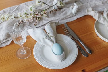 Paskalya brunch 'ı için şık bir ortam. Tavşan peçetesindeki paskalya yumurtası tabakta çatal bıçak, tavşan, bahar çiçekleri ve ahşap masada kırsal kumaş. Paskalya sofrası düzenleme ve çevre dostu dekorasyonlar