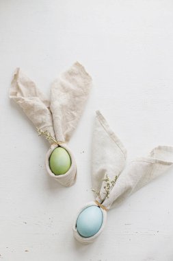 Paskalya yumurtaları tavşan peçetelerinde bahar çiçekleri ve kır beyazı masa manzaralı. Tatil masası düzenlemesi, kumaş dekorasyonunda doğal boya yumurtaları. Modern Paskalya brunch sofrası