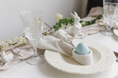 Tavşan peçetesinde paskalya yumurtası, çatal bıçak takımı, tavşan, kırsal beyaz masa üzerinde bahar çiçekleri. Zarif Paskalya brunch sofrası. Modern tablo düzenleme ve eko dekorasyon