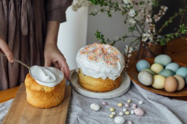 Ev yapımı paskalya ekmeğini köy masasında şeker jöleli yumurta ve bahar çiçeğiyle süsleyen bir kadın. Mutlu Paskalyalar! Paskalya pastası pişiren kadın.