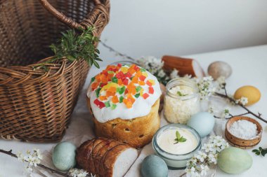Paskalya ekmeği ve kırsal masada bahar çiçeği ve hasır sepetli doğal boyalı yumurtalar. Geleneksel Paskalya sepeti yiyeceği - kremalı ve şekerli Paskalya pastası, yumurta, jambon, pancar, tereyağı.