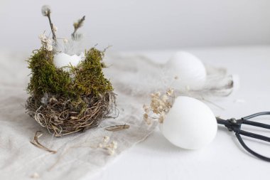 Happy Easter! Easter rustic still life. Easter egg shells with pussy willow branches, feathers and flowers in nest on aged table. Stylish festive decoration on table. Space for text