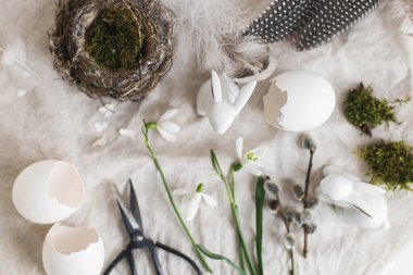 Paskalya kırsalında hayat. Paskalya yumurtası kabukları, çiçek açan kardelenler, tavşan heykelcikleri, yuva ve tüyler bez kumaşın üzerinde düzdü. Masada sade bir şenlik süsü var. Mutlu Paskalyalar