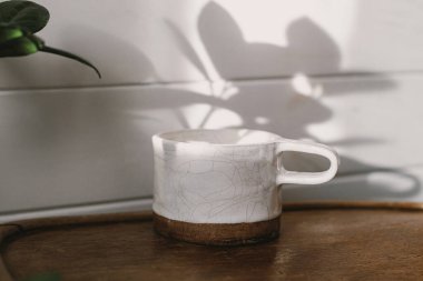 Kırsal arka planda güneş ışığında şık bir bardak. Modern seramik minimalist fincan ahşap sandalyede ve şık, güneşli boho odasında gölge bırakır. Sabah kahvesi estetiği.