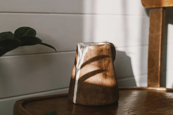 ホーム美学 素朴な木製の椅子に日光の近代的なセラミックケトルと影を残します 植物と日当たりの良いブースルームでスタイリッシュなセラミックミニマリスト花瓶 — ストック写真