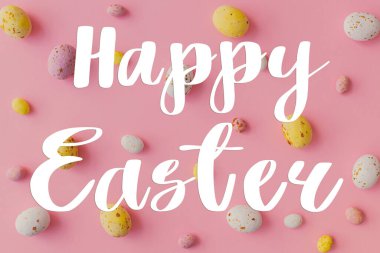 Mutlu Paskalya tebrik kartları. Mutlu Paskalya metinleri ve pembe arka planda duran renkli çikolata yumurtaları. Mevsimlik tebrik kartı, el yazması mektuplar.