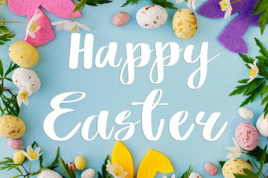 Mutlu Paskalya tebrik kartları. Mutlu Paskalya metinleri, renkli tavşanlar, çikolatalı yumurtalar ve mavi arka planda bahar çiçekleri çerçevesi, düz yatak. Mevsimlik tebrik kartı, el yazması mektuplar.