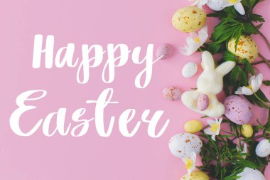 Mutlu Paskalya tebrik kartları. Mutlu Paskalya metinleri ve Paskalya çikolataları, tavşanlar ve bahar çiçekleri pembe arka planda yatıyordu. Mevsimlik tebrik kartı, el yazması mektuplar.