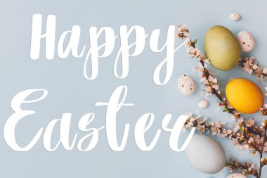 Mutlu Paskalya tebrik kartları. Mutlu Paskalya metinleri ve modern stil mavi ve sarı paskalya yumurtaları, kiraz çiçekleri mavi arka planda yatıyordu. Mevsimlik tebrik kartı, el yazması mektuplar.