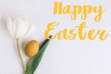 Mutlu Paskalya tebrik kartları. Mutlu Paskalya metinleri ve şık sarı Paskalya yumurtası ve lale düz beyaz ahşap üzerinde yatıyordu. Mevsimlik tebrik kartı, el yazması mektuplar.