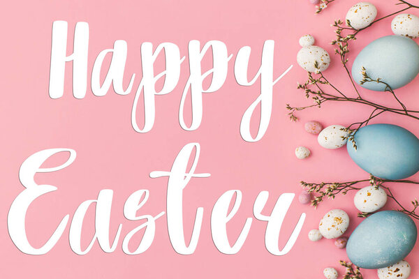 Happy Easter greeting card. Happy Easter text and modern Easter eggs and flower flat lay on pink background. Seasons greeting card, handwritten lettering