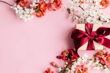 Pembe arka planda çiçekli şık bir hediye kutusu. Anneler Günün kutlu olsun. Tebrik kartı şablonu metin için boşluk ile birlikte. Kurdeleli el yapımı hediye, kırmızı çiçekler ve kiraz çiçeği sınır kompozisyonu