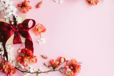 Pembe arka planda çiçekli şık bir hediye kutusu. Anneler Günün kutlu olsun. Tebrik kartı şablonu metin için boşluk ile birlikte. Kurdeleli el yapımı hediye, kırmızı çiçekler ve kiraz çiçeği sınır kompozisyonu
