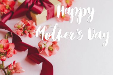 Anneler Günün kutlu olsun. Mutlu anneler günü mesajı ve pembe arka planda kırmızı çiçekli hediye kutusu. Şık bir çiçek tebrik kartı. El yazısıyla yazılmış harfler. Anneler Günü